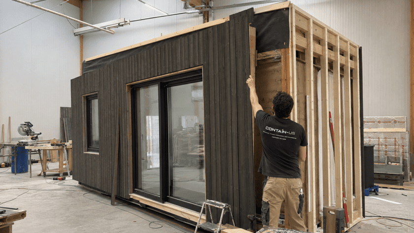 Mitarbeiter montiert die Holzfassade an einem Modul in der Werkstatt von Contain-us in Landsberg am Lech