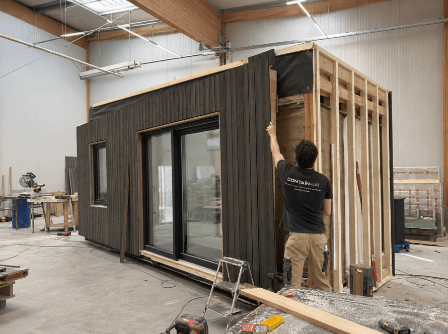 Mitarbeiter montiert die Holzfassade an einem Modul in der Werkstatt von Contain-us in Landsberg am Lech