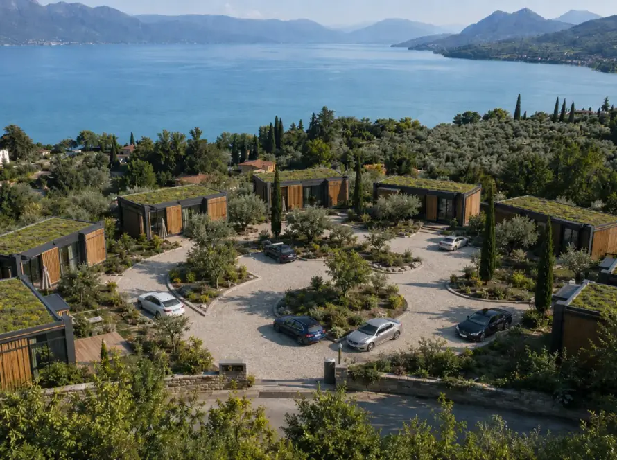 Luftaufnahme einer Ferienanlage aus Modulhäusern mit begrünten Dächern über einem See mit Bergpanorama