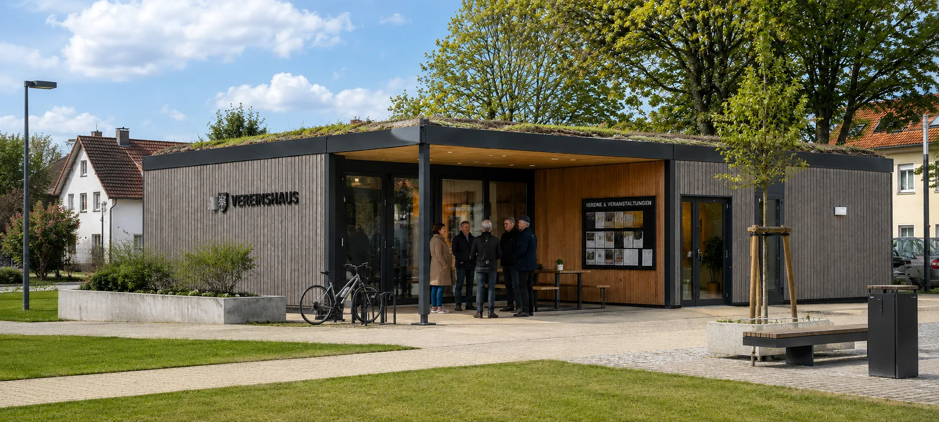 Vereinshaus in Modulbauweise mit überdachtem Vorbereich und Schaukasten, davor stehen mehrere Personen