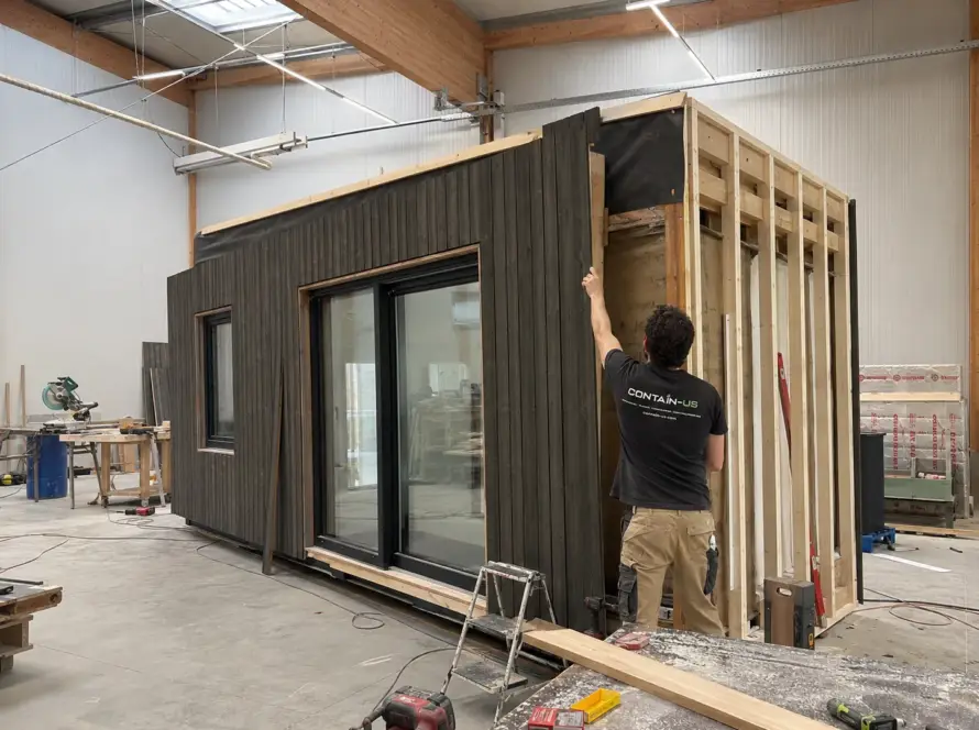 Mitarbeiter montiert die Holzfassade an einem Modul in der Werkstatt von Contain-us in Landsberg am Lech