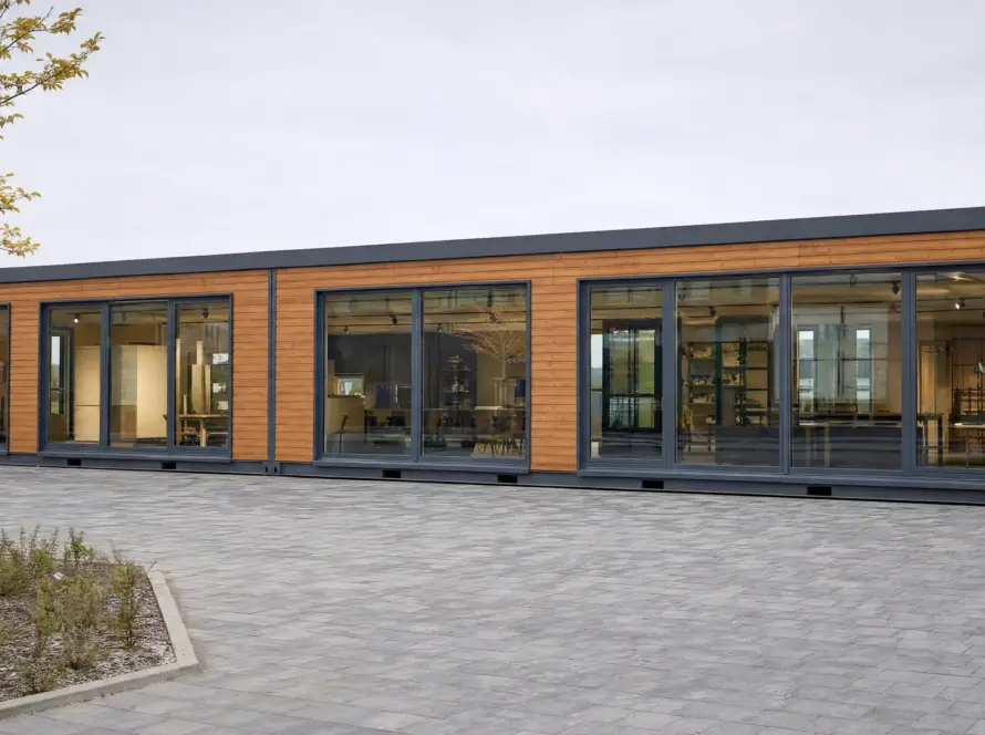 Langgestrecktes eingeschossiges Gewerbegebäude in Modulbauweise mit Lärchenholzfassade und raumhohen Fensterfronten, davor ein gepflasterter Vorplatz