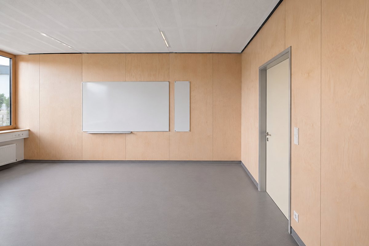 Leeres Klassenzimmer mit Wandbekleidung aus hellem Sperrholz, Whiteboard, grauem Boden und heller Tür