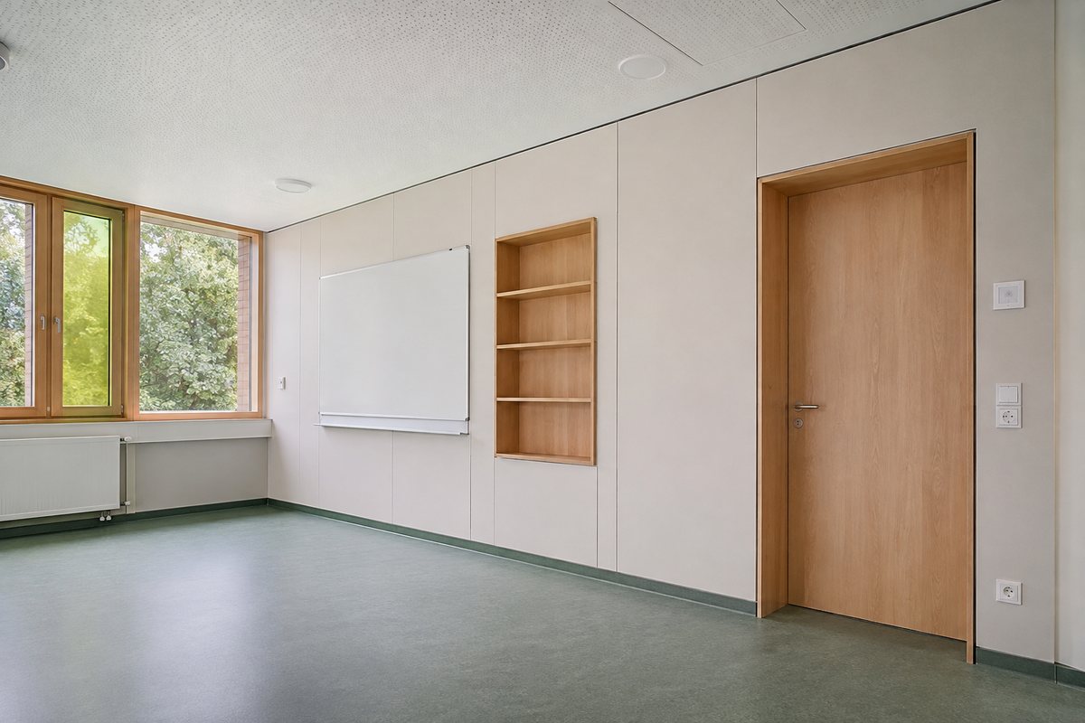 Leeres Klassenzimmer mit beigen Wandplatten, eingebauter Regalnische aus Holz, Whiteboard, grüngrauem Boden und Holztür