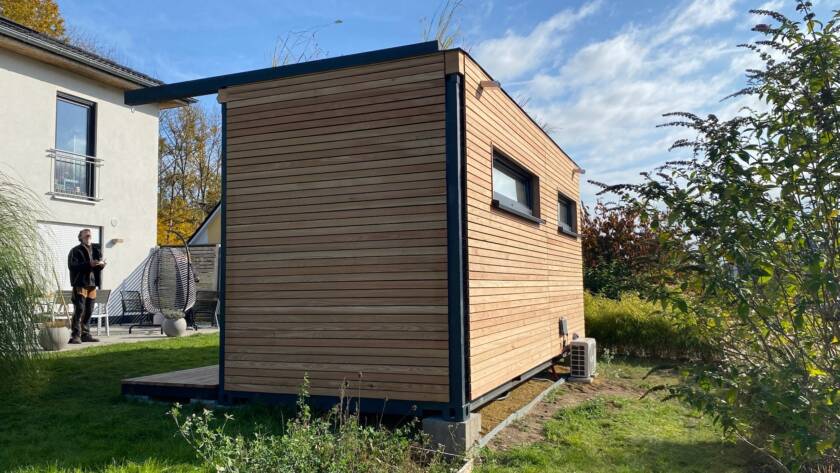 Fertiges Gartenbüro mit Lärchenholzfassade und Gründach, es steht sichtbar auf Betonsockeln neben dem Wohnhaus