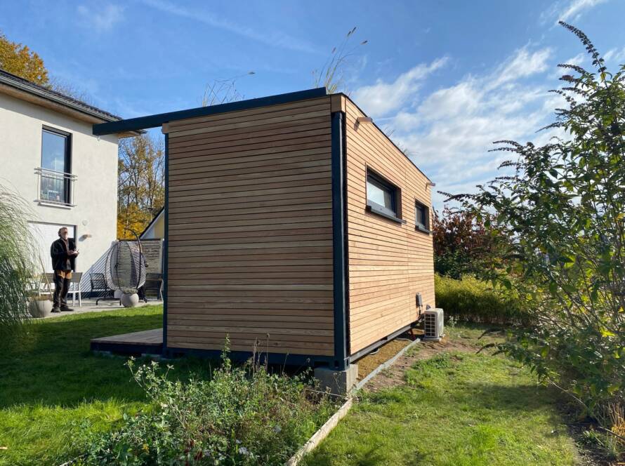 Fertiges Gartenbüro mit Lärchenholzfassade und Gründach, es steht sichtbar auf Betonsockeln neben dem Wohnhaus