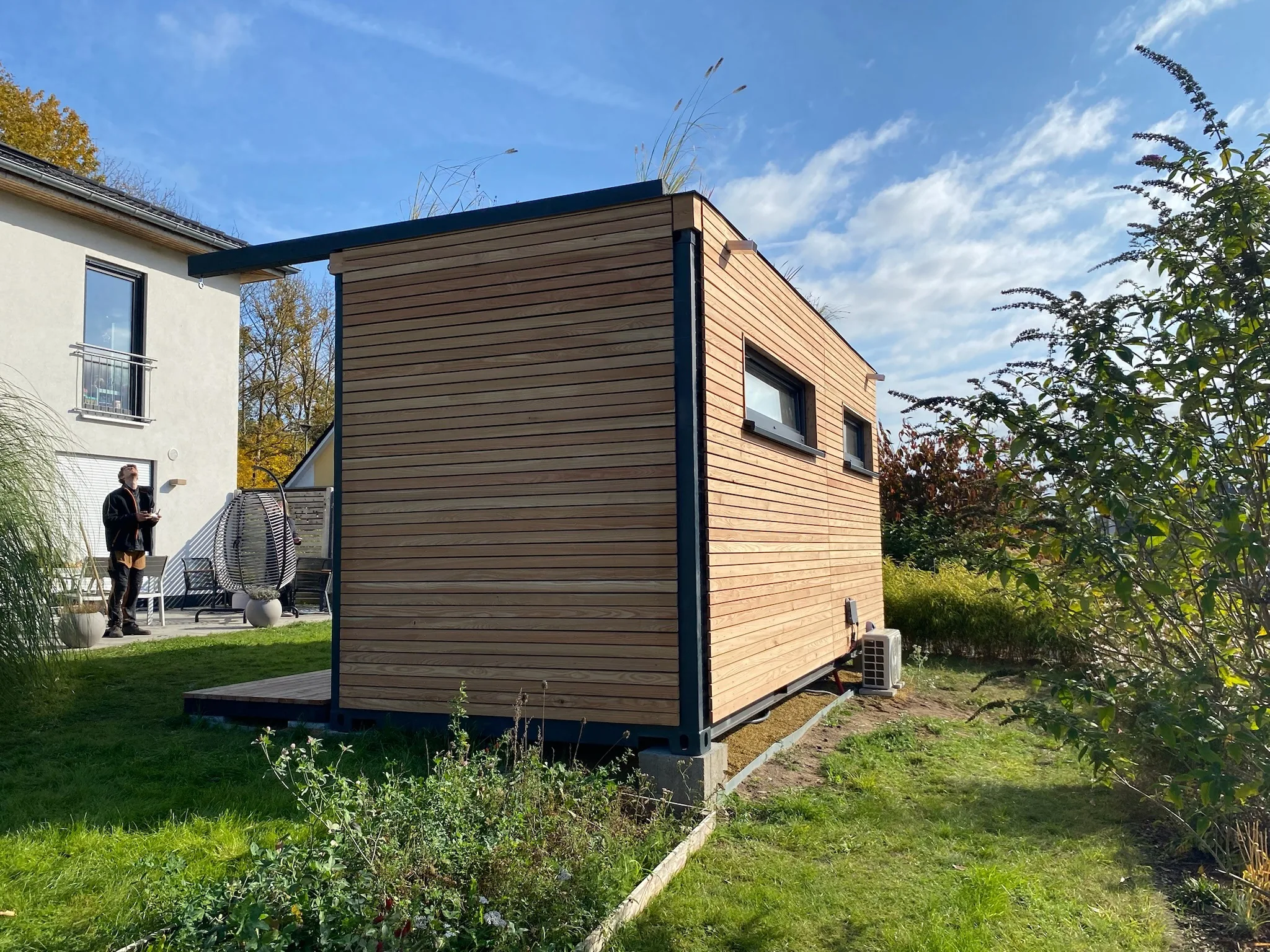 Fertiges Gartenbüro mit Lärchenholzfassade und Gründach, es steht sichtbar auf Betonsockeln neben dem Wohnhaus