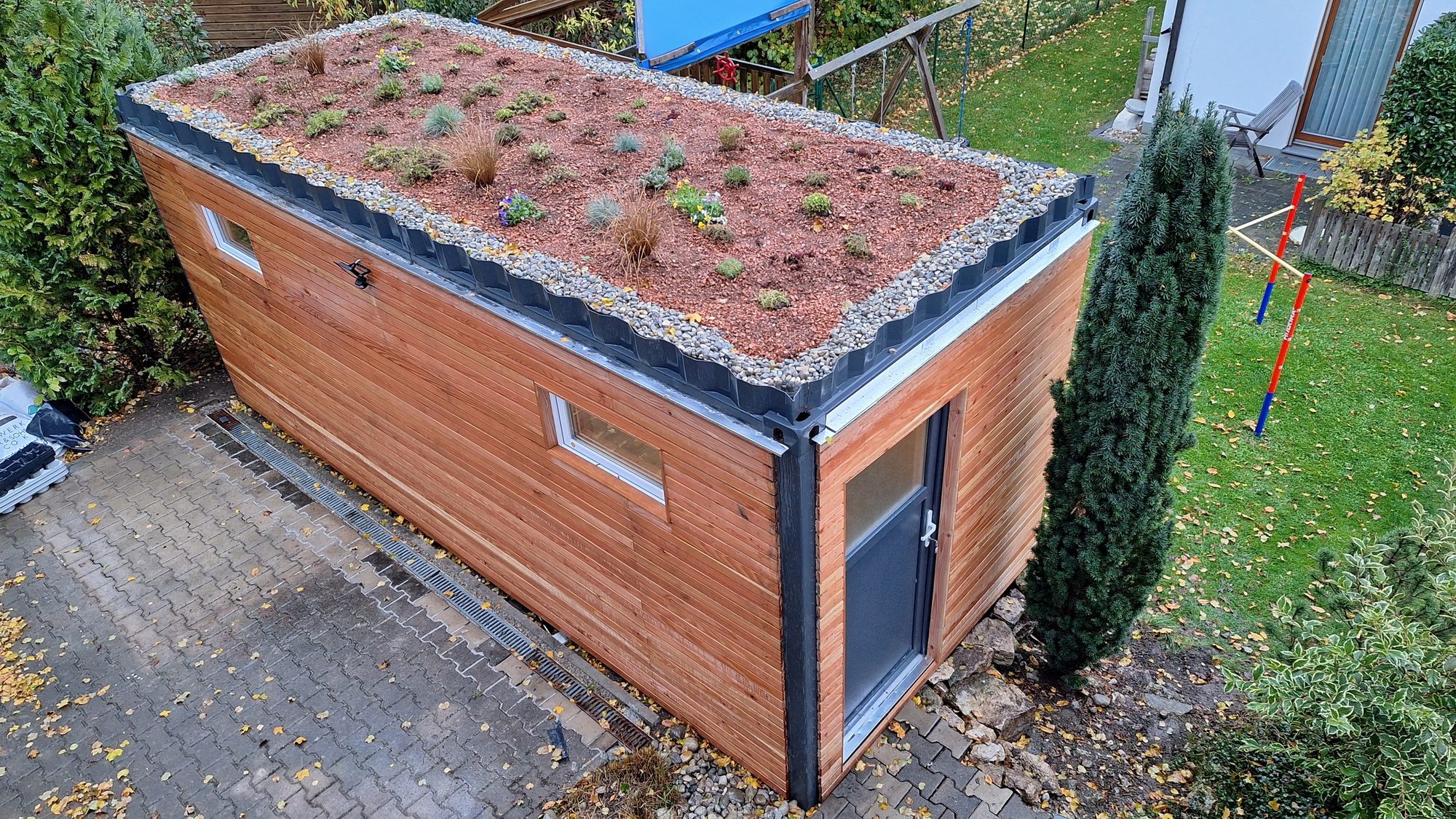 Gartenhaus 15 m² von Contain-us – Außenansicht mit begrüntem Dach auf einer gepflasterten Fläche