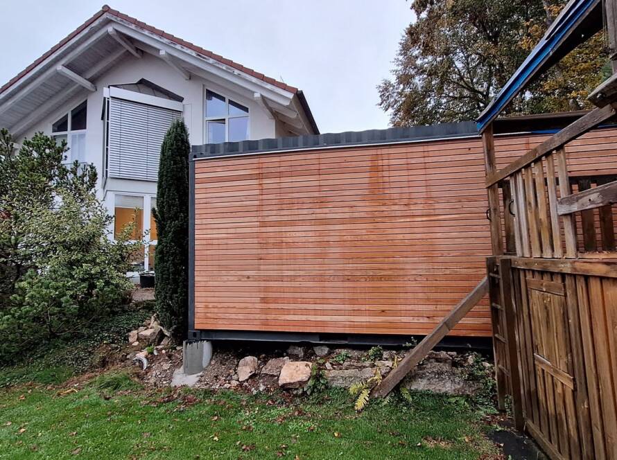 Gartenhaus 15 m² von Contain-us – das Modul steht auf Stützen hinter einem Holzzaun, die Höhe wird ausgerichtet