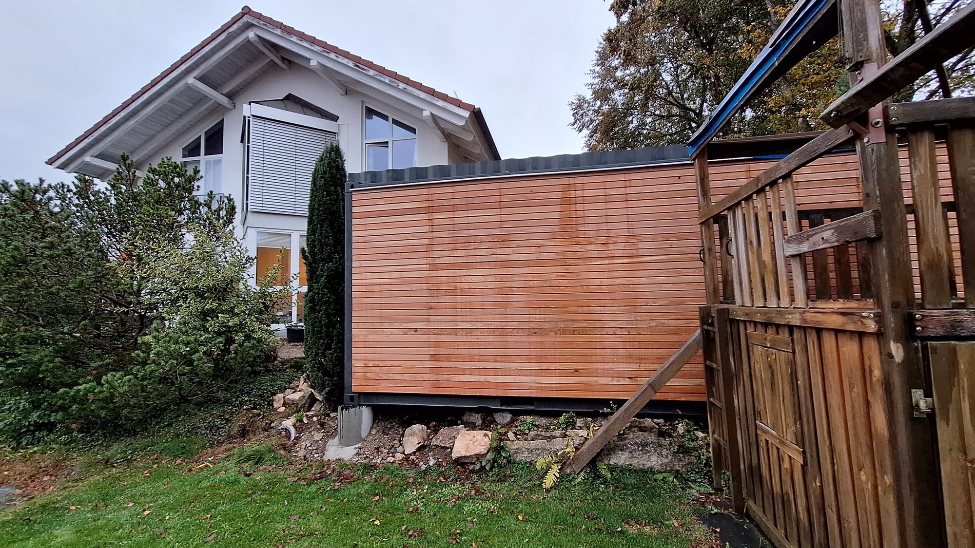 Gartenhaus 15 m² von Contain-us – das Modul steht auf Stützen hinter einem Holzzaun, die Höhe wird ausgerichtet