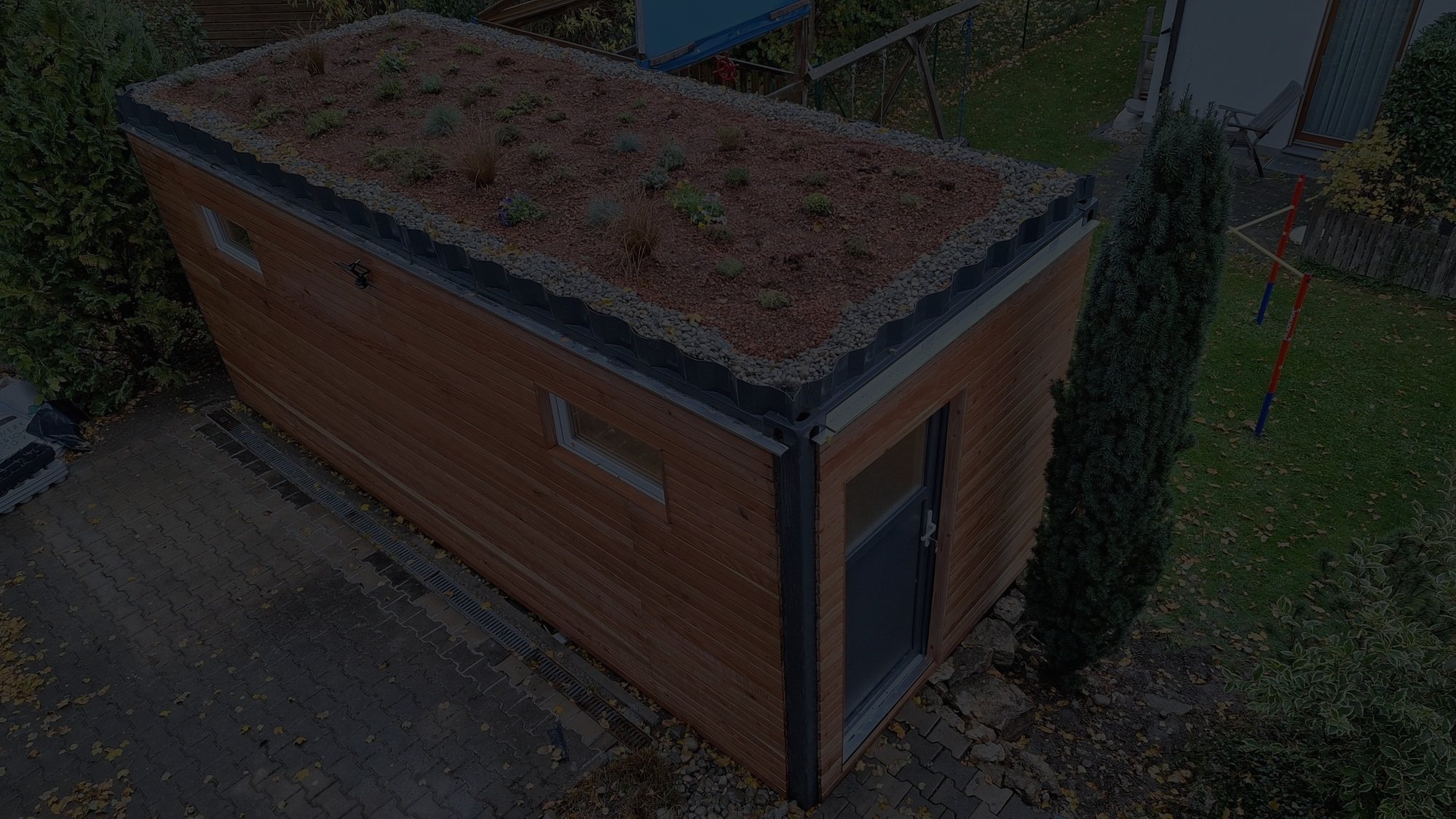 Gartenhaus 15 m² von Contain-us – Außenansicht mit begrüntem Dach auf einer gepflasterten Fläche