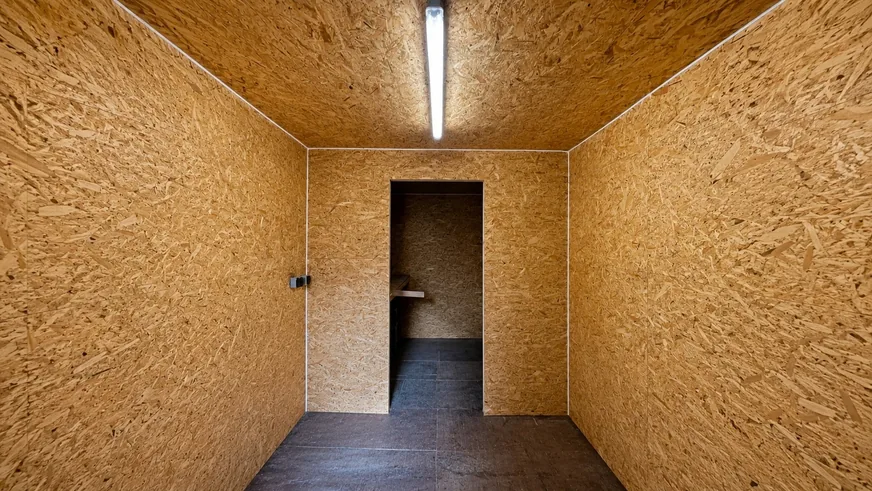 Mit OSB-Platten ausgebauter Innenraum, Blick durch die Tür in das zweite Abteil, an der Decke ein Feuchtraumstrahler