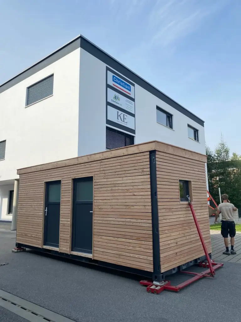 Gartenhaus 15 m² von Contain-us – das Modul steht auf Rangierrollen vor einem Wohnhaus und wird an seinen Platz geschoben