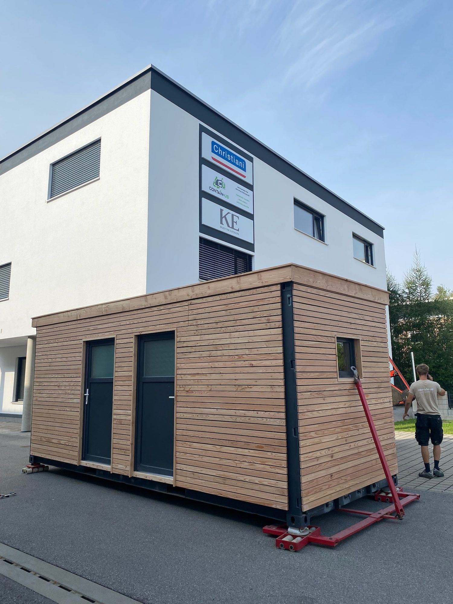 Gartenhaus 15 m² von Contain-us – das Modul steht auf Rangierrollen vor einem Wohnhaus und wird an seinen Platz geschoben