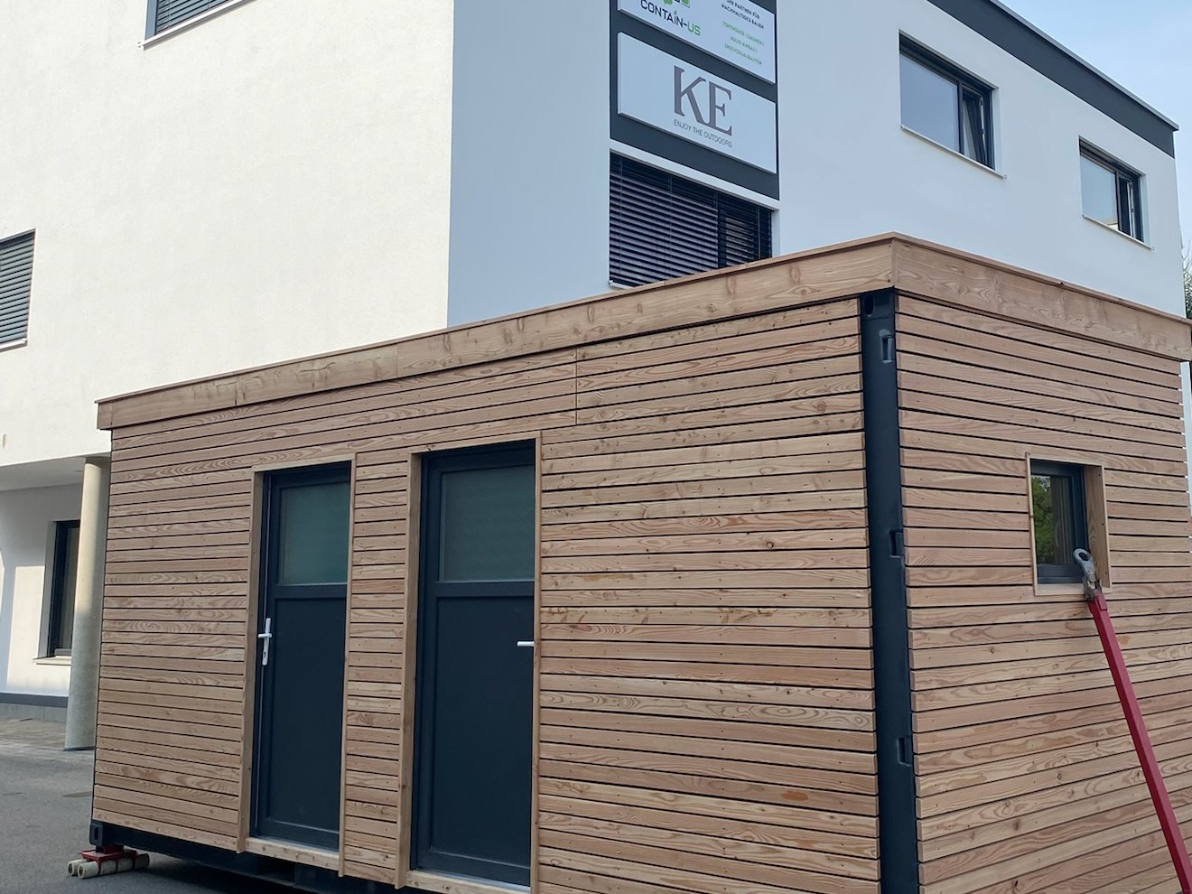 Gartenhaus 15 m² von Contain-us – Außenansicht neben einem Wohnhaus, helle Holzfassade mit zwei Türen