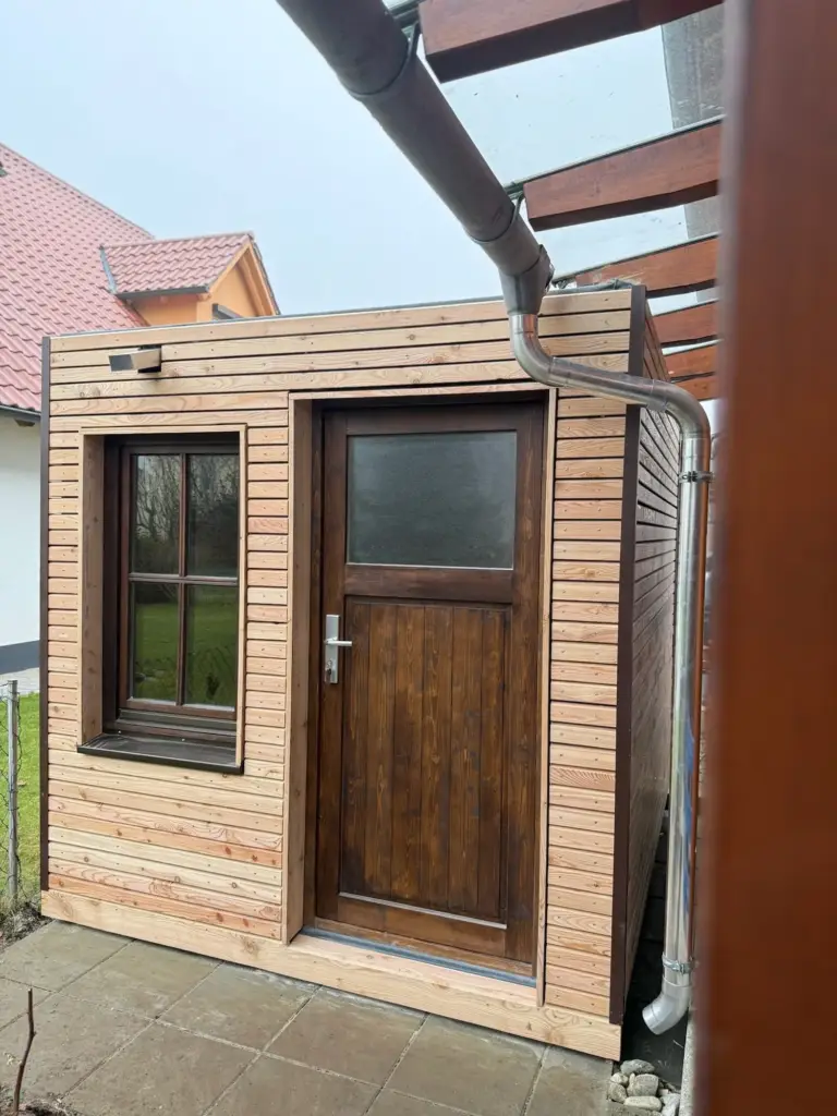 Gartenhaus 7 m² von Contain-us – Außenansicht mit Tür und Fenster, daneben ein Fallrohr