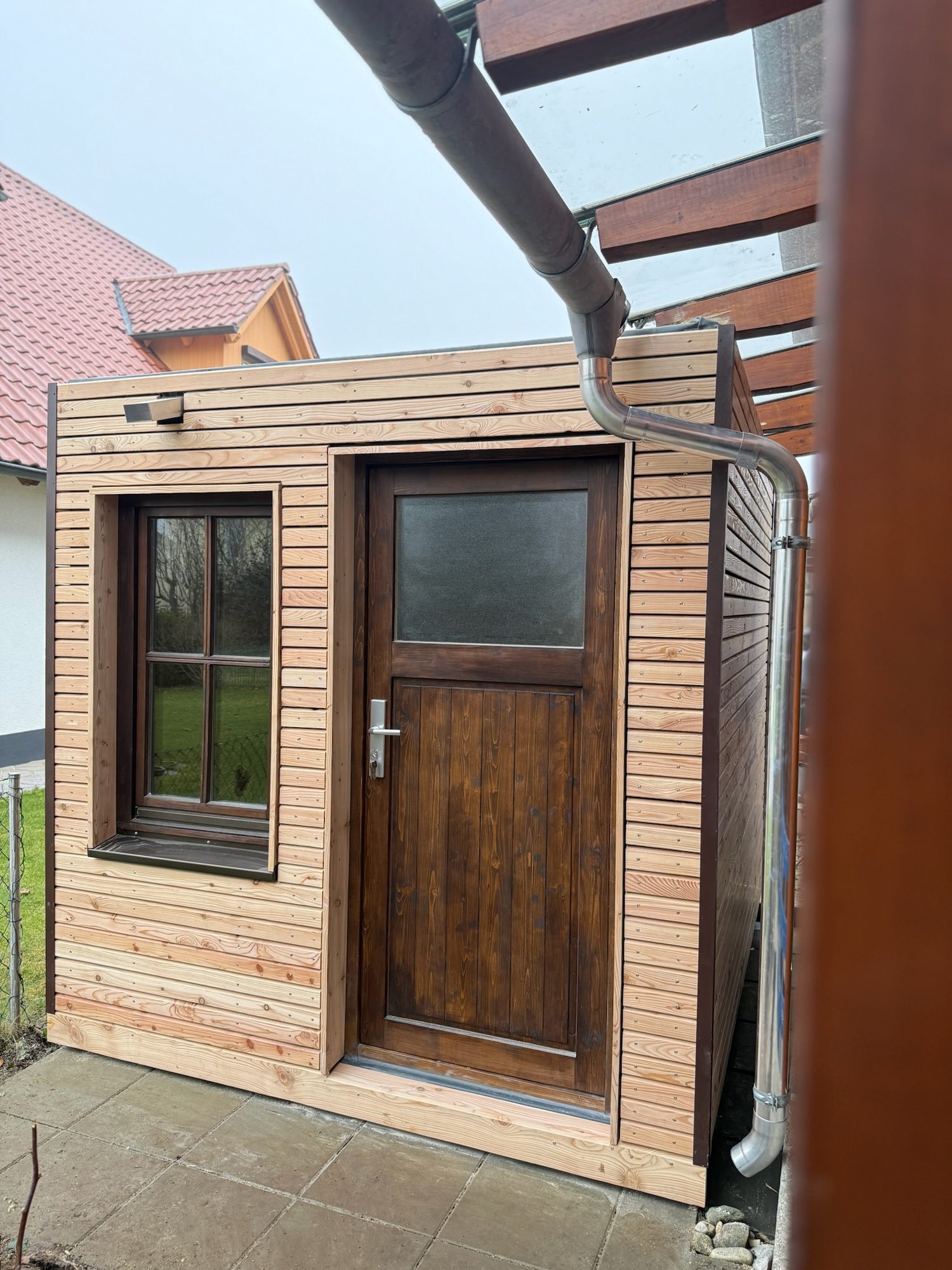 Gartenhaus 7 m² von Contain-us – Außenansicht mit Tür und Fenster, daneben ein Fallrohr