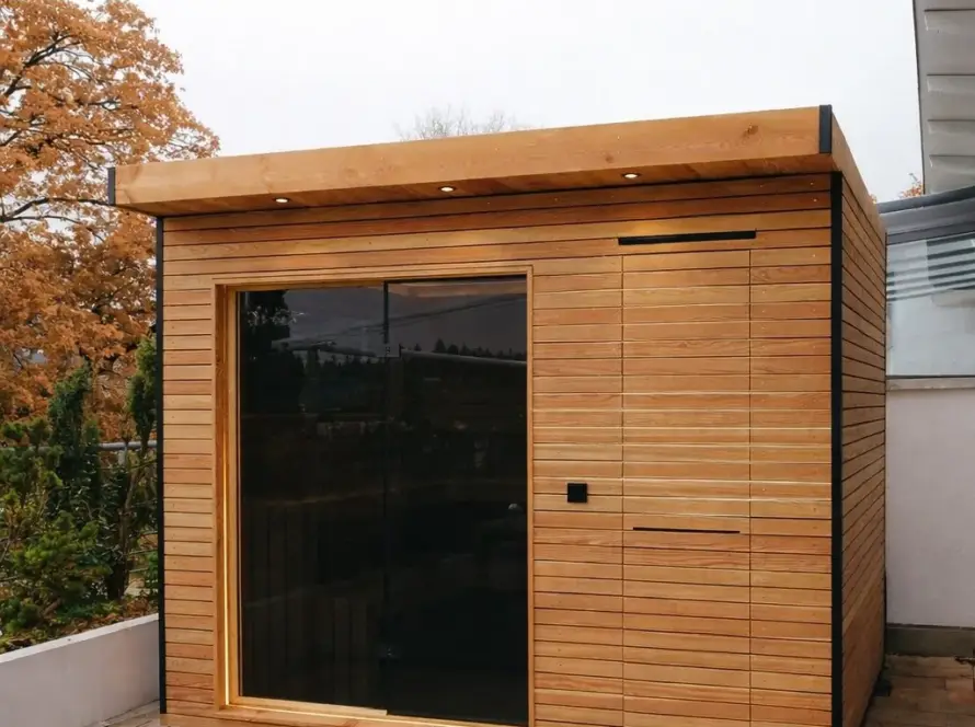 Sauna 7 m² von Contain-us – Außenansicht der Gartensauna auf einer gepflasterten Fläche, daneben ein Fenster zum Garten