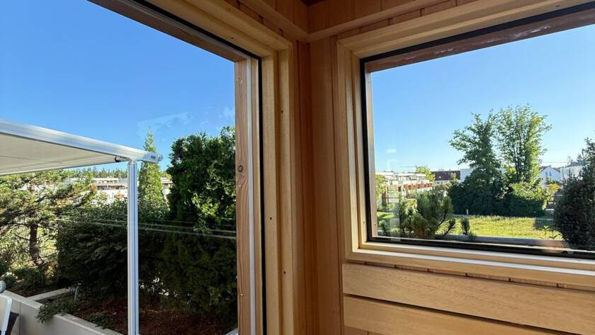 Sauna 7 m² von Contain-us – Blick von der Bank durch das Eckfenster in den Garten
