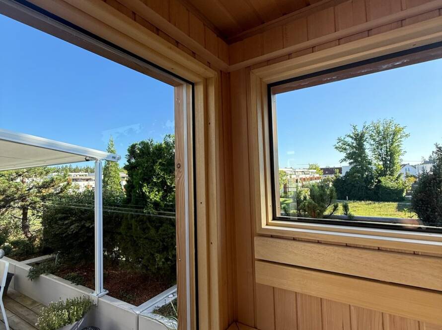 Sauna 7 m² von Contain-us – Blick von der Bank durch das Eckfenster in den Garten