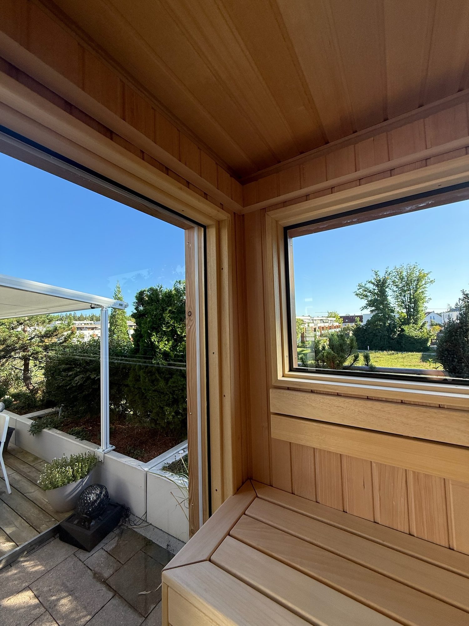 Sauna 7 m² von Contain-us – Blick von der Bank durch das Eckfenster in den Garten
