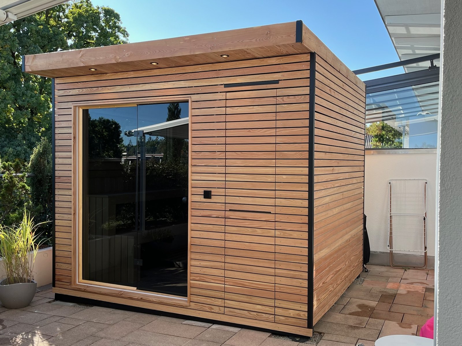 Sauna 7 m² von Contain-us – Außenansicht der freistehenden Gartensauna mit Panoramafenster und Holzfassade