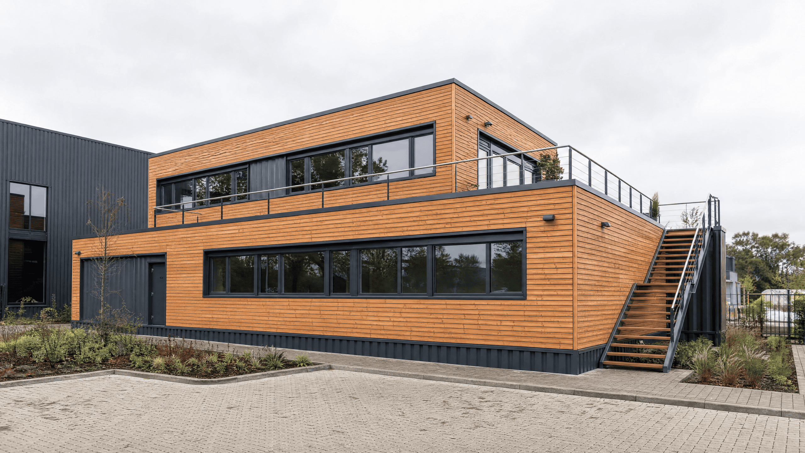 Zweigeschossiges Bürogebäude in Modulbauweise mit Holzfassade, Fensterband und Außentreppe