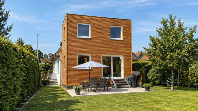 Hausanbau 60 m² von Contain-us – Blick von der Gartenseite auf den Anbau, davor Sonnenschirm und Sitzgruppe auf der Terrasse