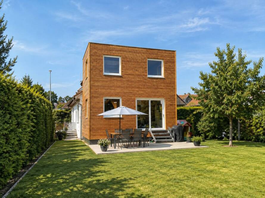 Hausanbau 60 m² von Contain-us – Blick von der Gartenseite auf den Anbau, davor Sonnenschirm und Sitzgruppe auf der Terrasse