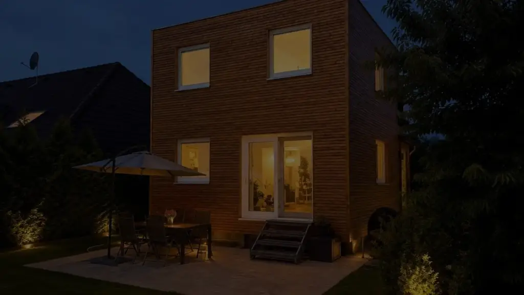 Hausanbau 60 m² von Contain-us – der Anbau in der Dämmerung, die Fenster sind warm beleuchtet, auf der Terrasse steht eine Sitzgruppe