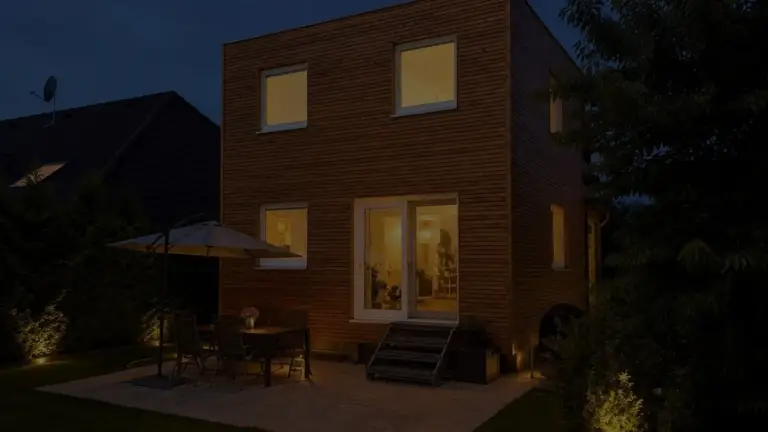 Hausanbau 60 m² von Contain-us – der Anbau in der Dämmerung, die Fenster sind warm beleuchtet, auf der Terrasse steht eine Sitzgruppe