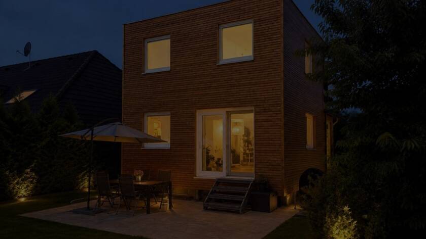 Hausanbau 60 m² von Contain-us – der Anbau in der Dämmerung, die Fenster sind warm beleuchtet, auf der Terrasse steht eine Sitzgruppe