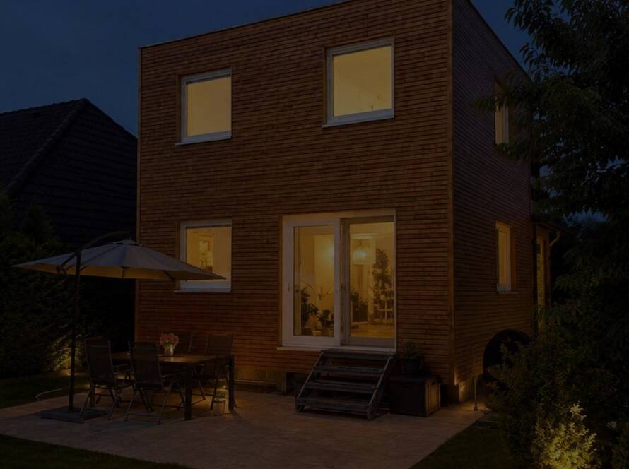 Hausanbau 60 m² von Contain-us – der Anbau in der Dämmerung, die Fenster sind warm beleuchtet, auf der Terrasse steht eine Sitzgruppe