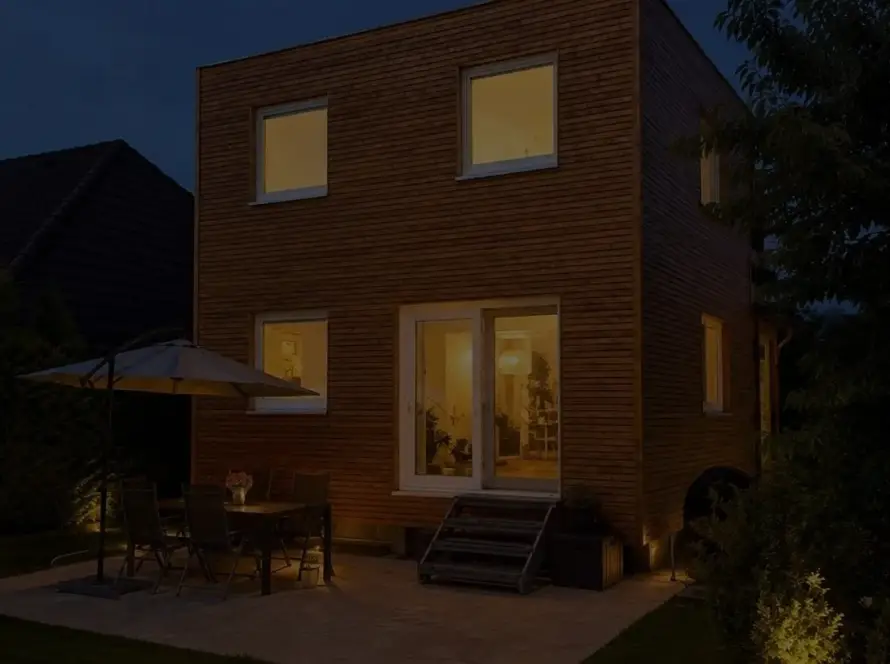 Hausanbau 60 m² von Contain-us – der Anbau in der Dämmerung, die Fenster sind warm beleuchtet, auf der Terrasse steht eine Sitzgruppe