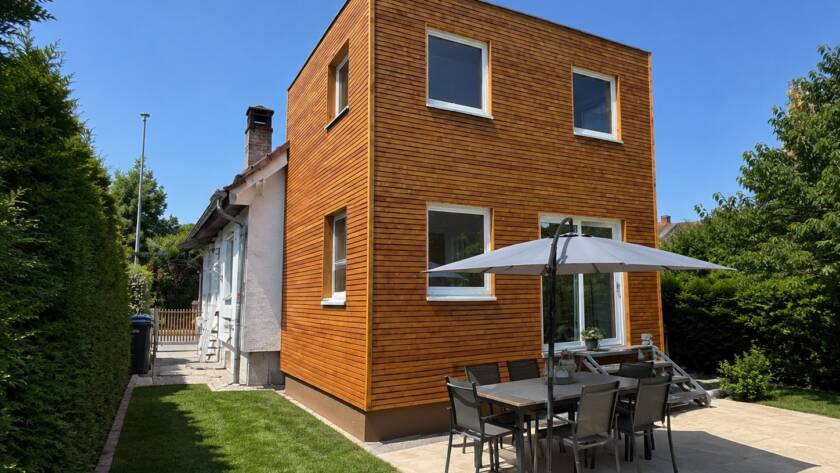 Hausanbau 60 m² von Contain-us – Außenansicht des zweigeschossigen Anbaus mit Terrasse und Sonnenschirm