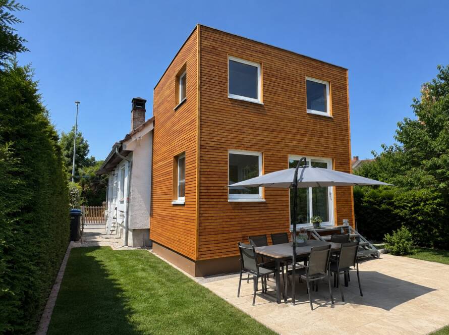 Hausanbau 60 m² von Contain-us – Außenansicht des zweigeschossigen Anbaus mit Terrasse und Sonnenschirm
