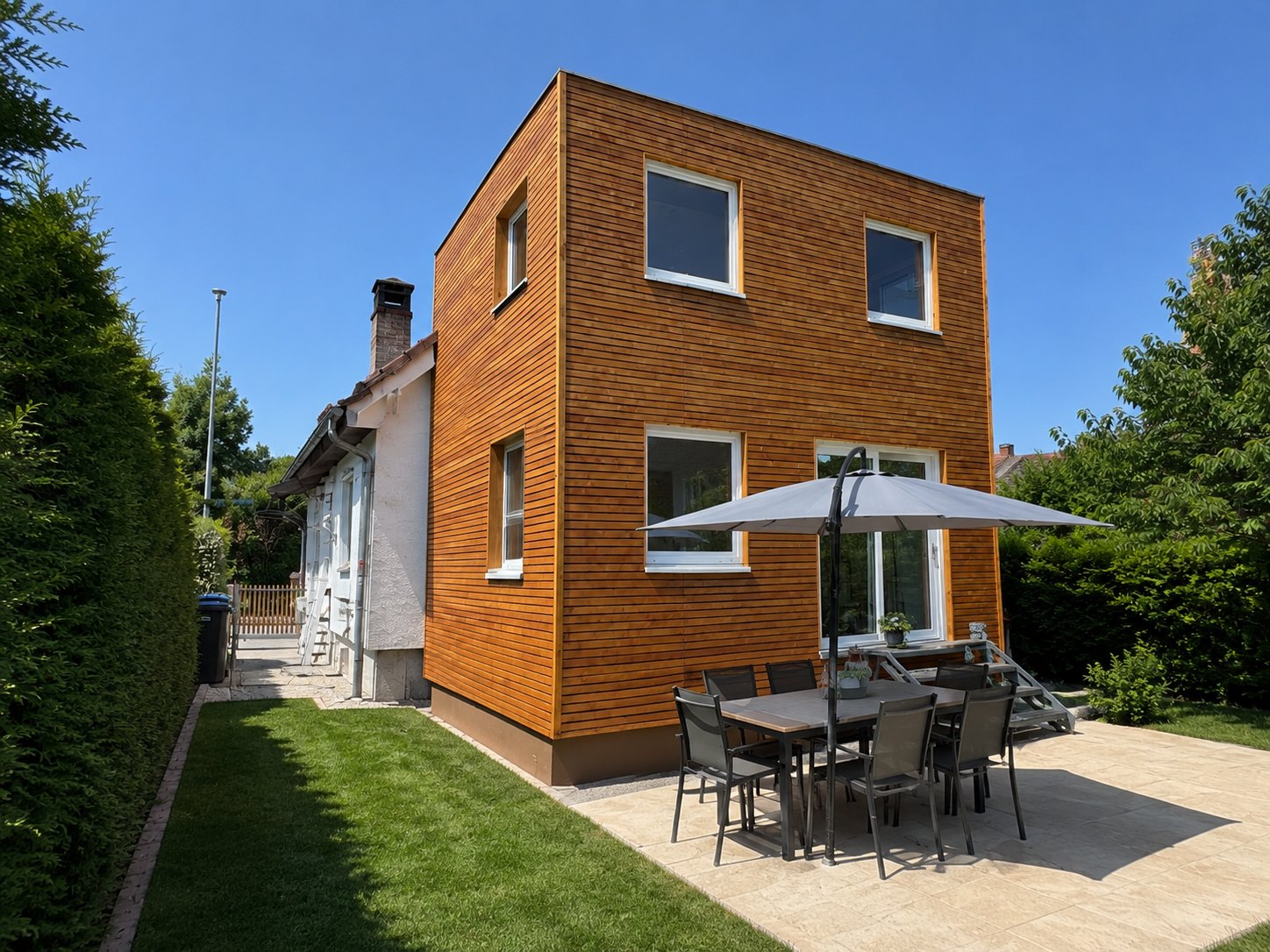 Hausanbau 60 m² von Contain-us – Außenansicht des zweigeschossigen Anbaus mit Terrasse und Sonnenschirm