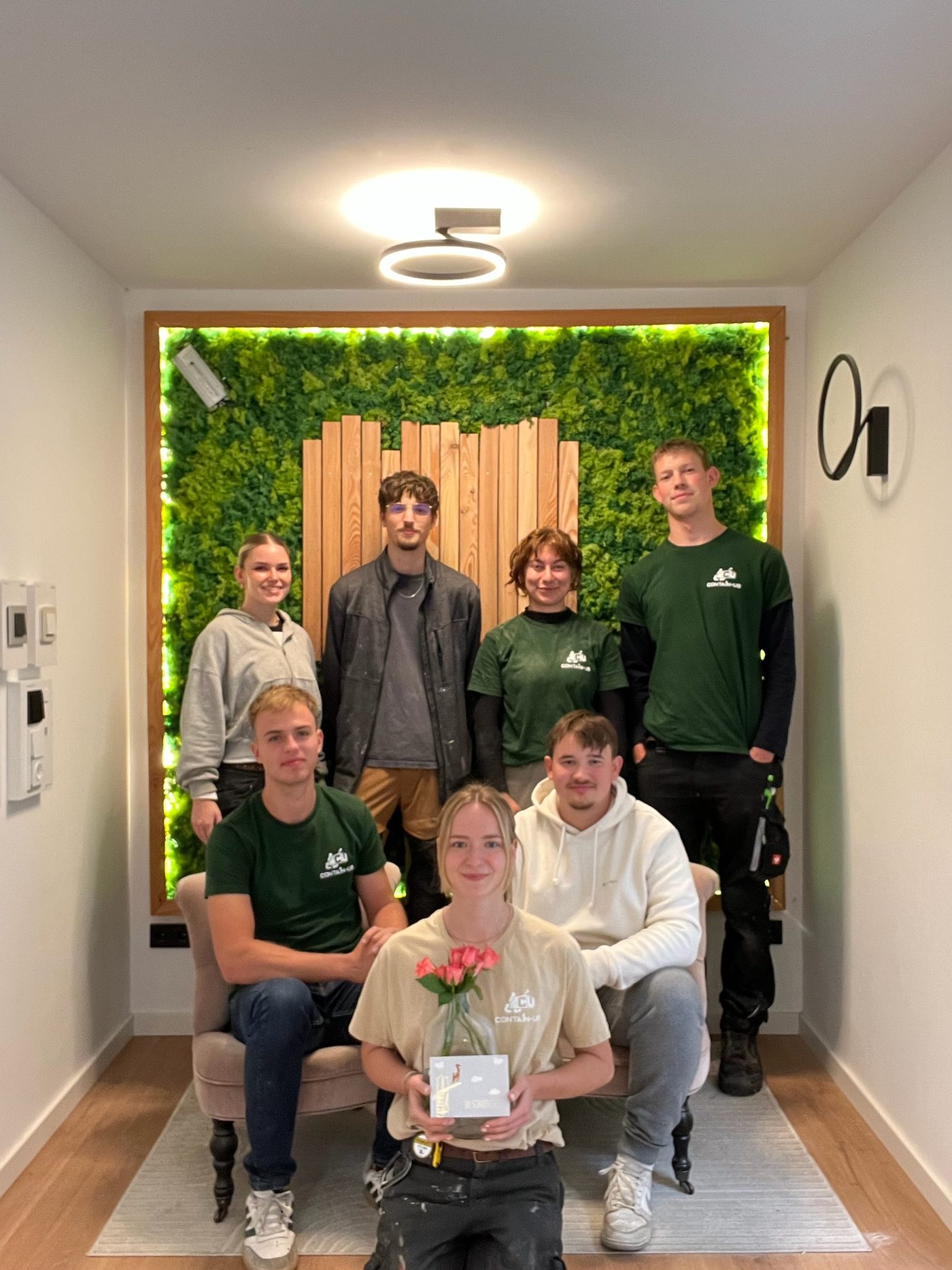 Sieben Teammitglieder in einem fertig ausgebauten Modul mit beleuchteter Mooswand und Holzverkleidung