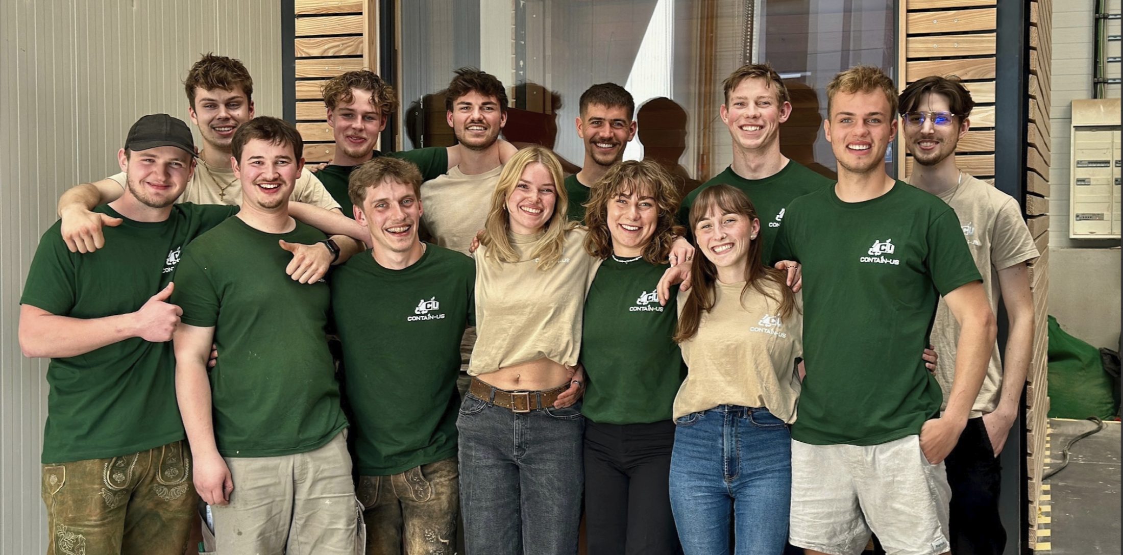 Das Team von Contain-us steht nebeneinander in der Fertigungshalle, die meisten in grünen Firmen-Shirts