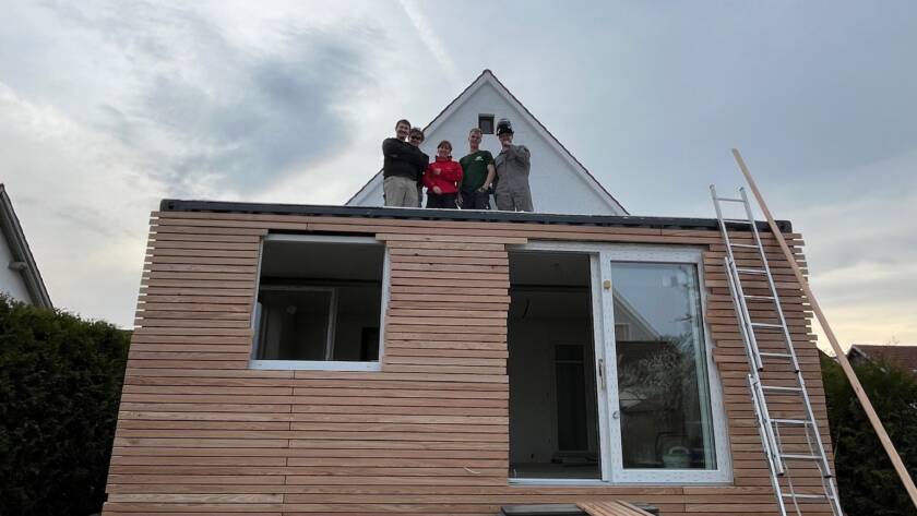 Modul auf einem Streifenfundament mit Kiesbett, das Montageteam steht auf dem Dach, die Fassade ist teilweise verlattet