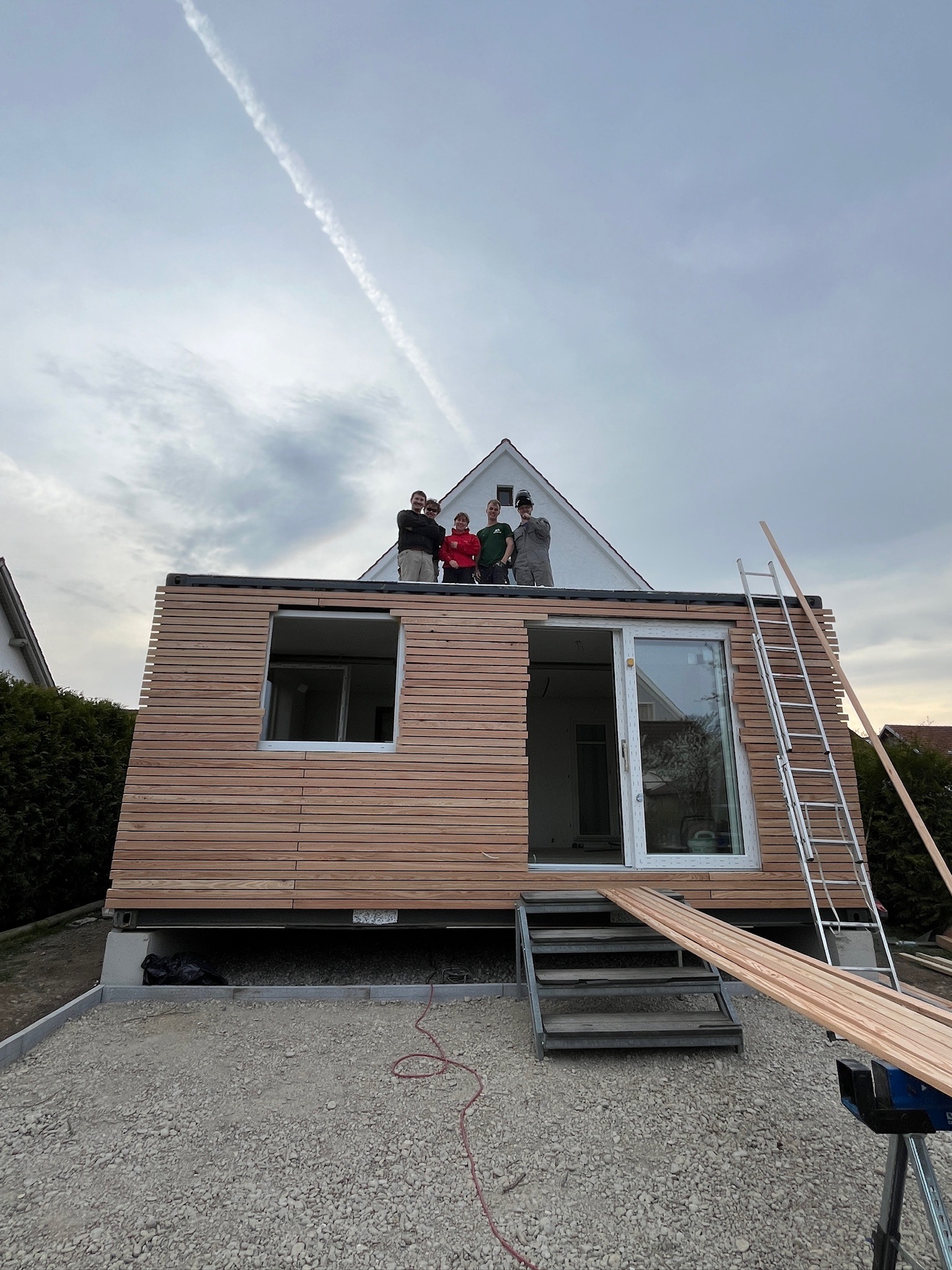 Modul auf einem Streifenfundament mit Kiesbett, das Montageteam steht auf dem Dach, die Fassade ist teilweise verlattet