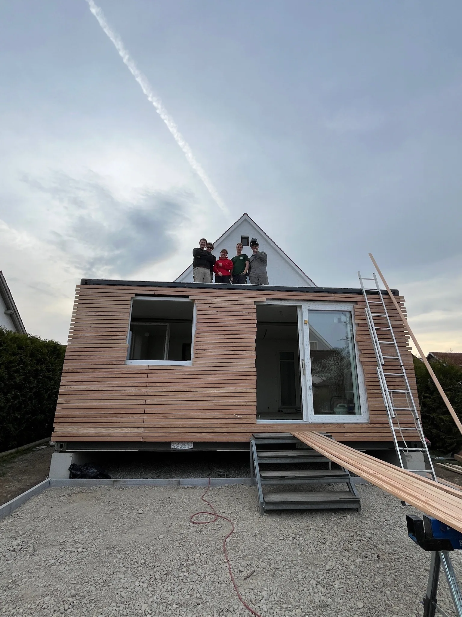 Modul auf einem Streifenfundament mit Kiesbett, das Montageteam steht auf dem Dach, die Fassade ist teilweise verlattet