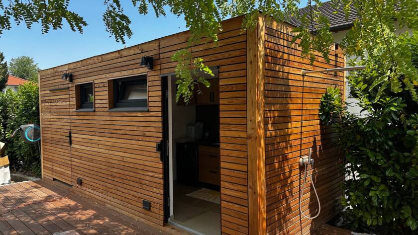 Poolhaus von Contain-us – Außenansicht mit Holzfassade und geöffneter Tür, davor eine gepflasterte Fläche