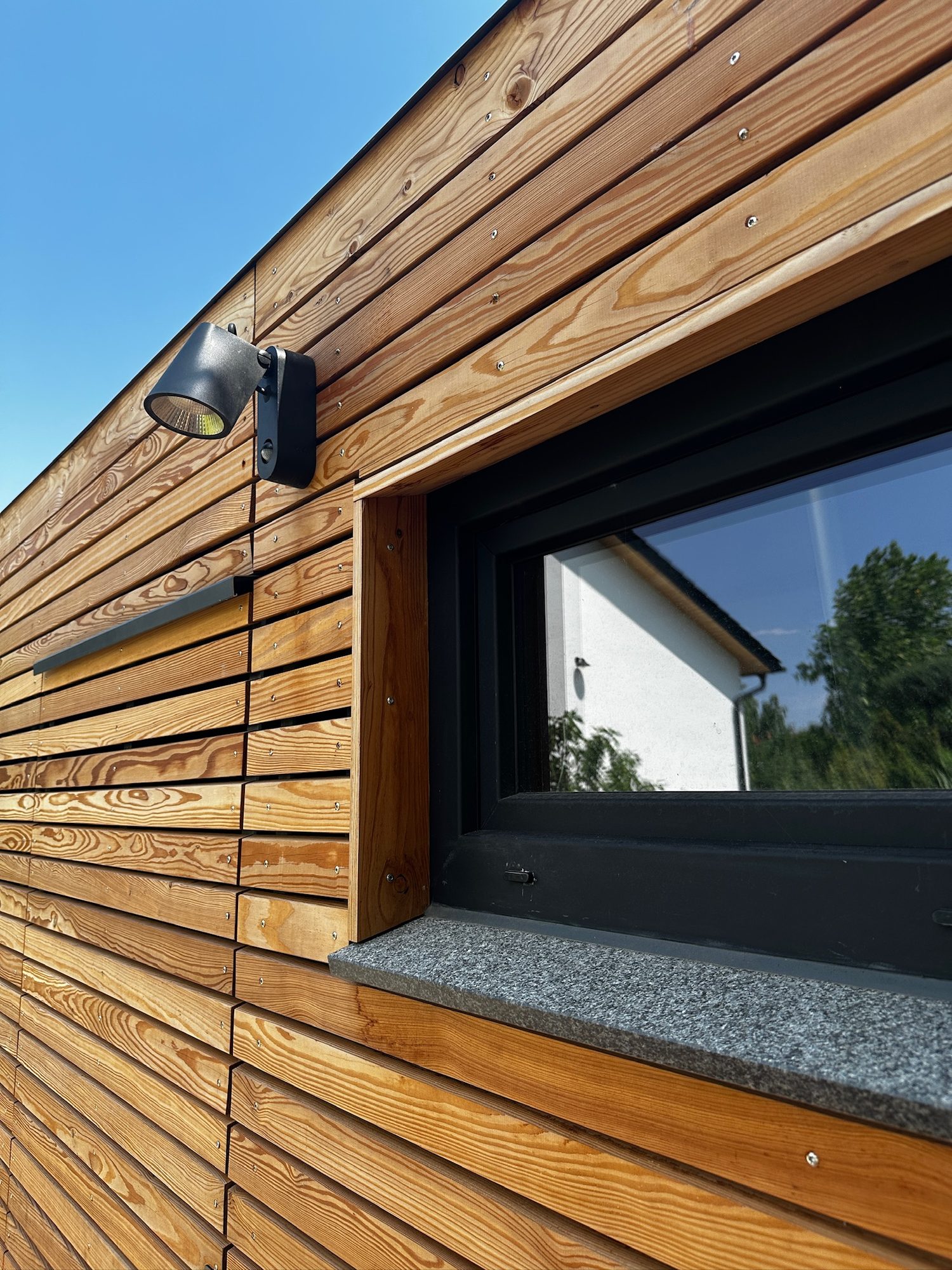 Poolhaus von Contain-us – Detail der Holzfassade mit Fenster und Wandleuchte