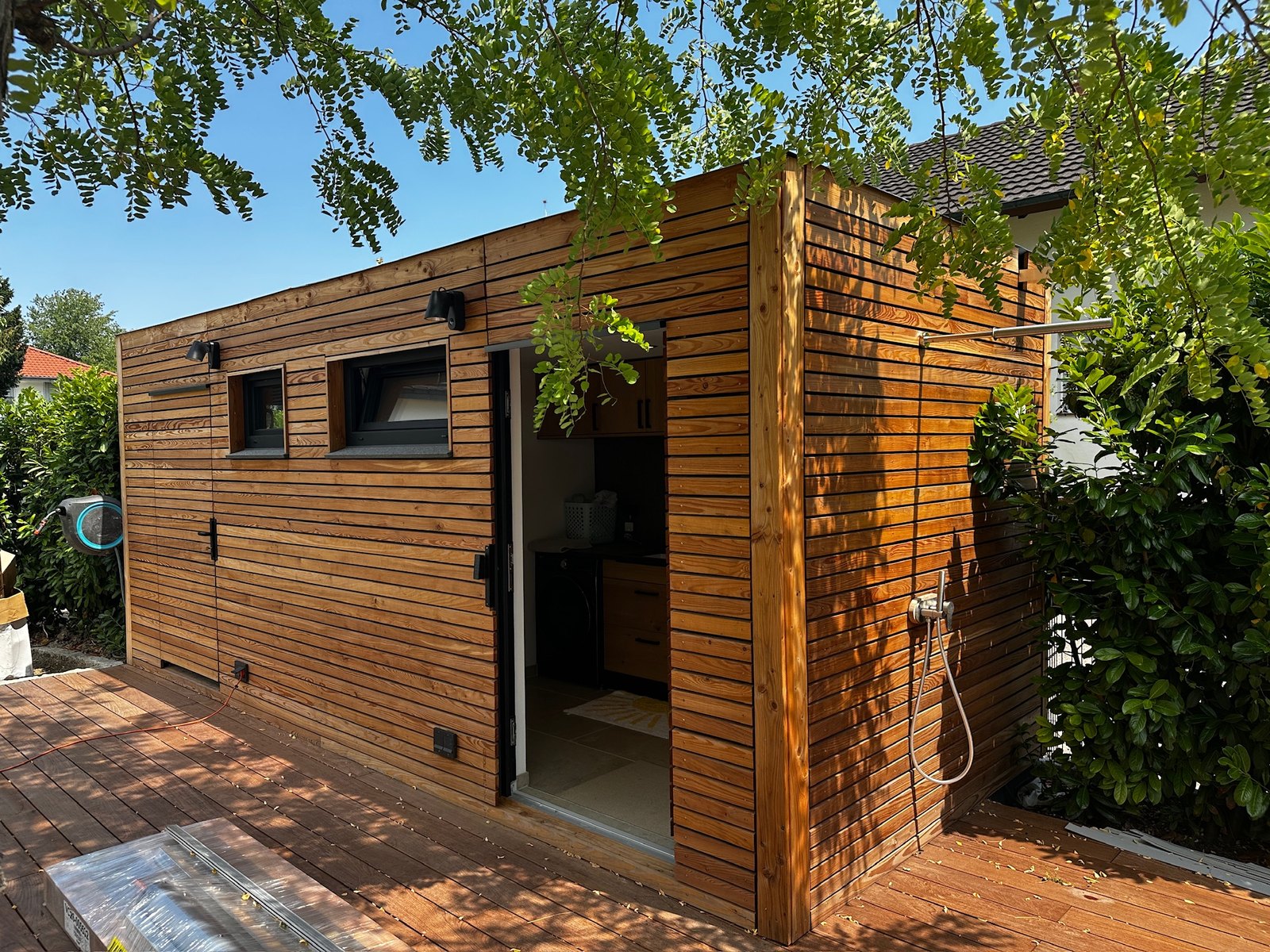 Poolhaus von Contain-us – Außenansicht mit geöffneter Tür und Außendusche an der Holzfassade