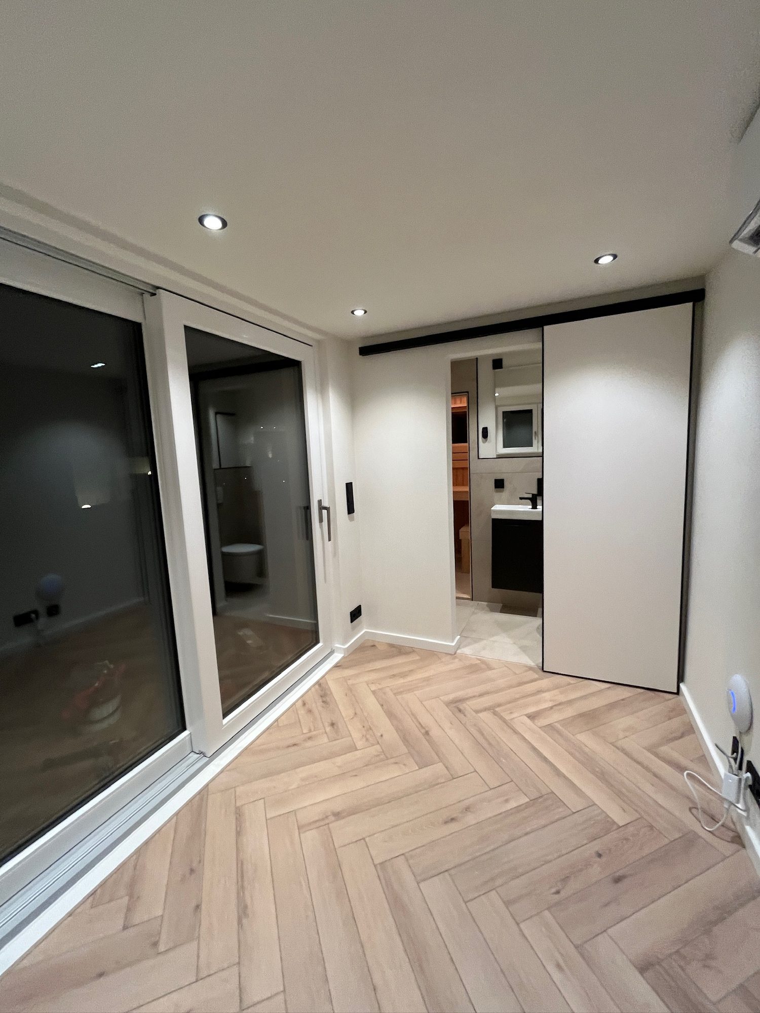 Sauna mit Büro 15 m² von Contain-us – Blick durch die geöffnete Tür auf den Innenraum mit Fischgrätboden