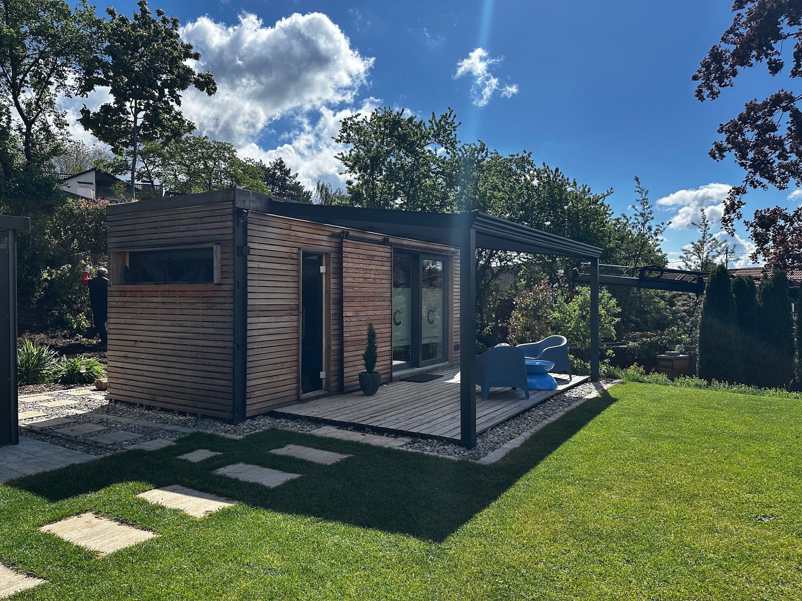 Sauna mit Büro 15 m² von Contain-us – Außenansicht mit Glasfront, davor eine gepflasterte Terrasse