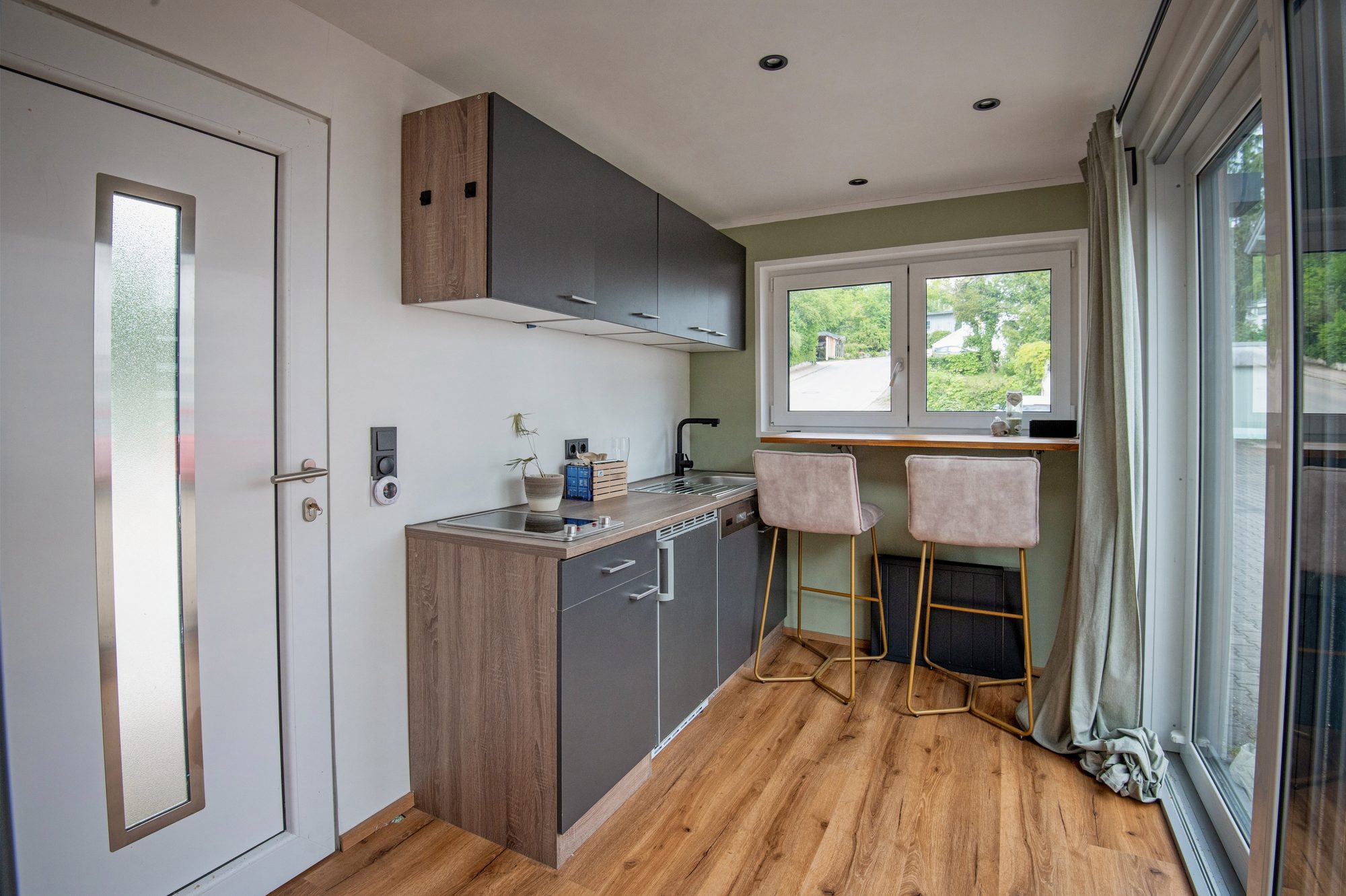 Tiny House 15 m² von Contain-us – Küchenzeile mit Arbeitsplatte, Hängeschränken und Eingangstür