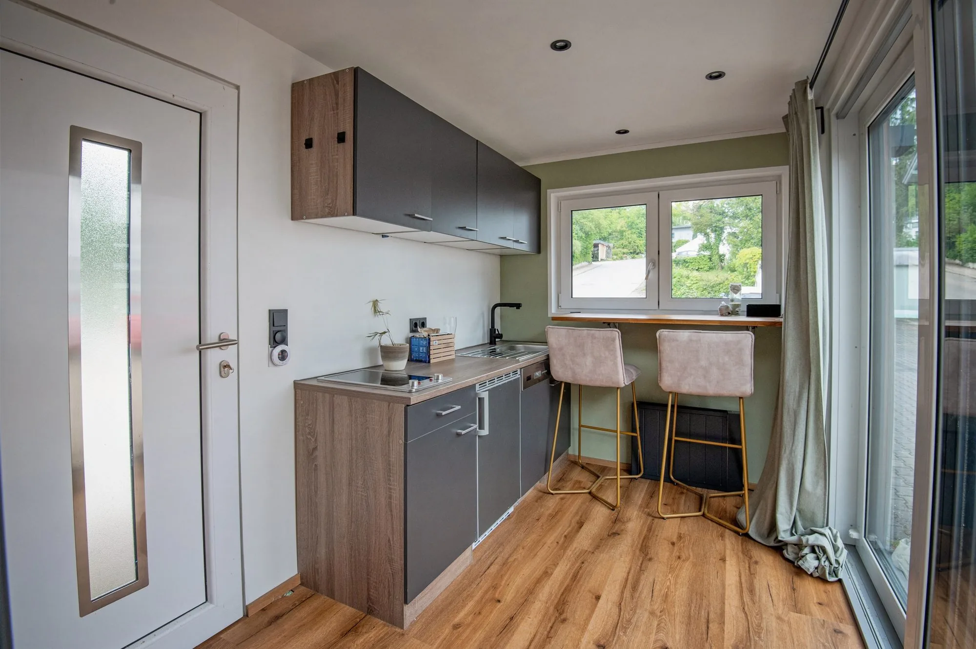 Kochzeile mit Geschirrspüler, Fenstertheke und zwei Barhockern in einem 15-m²-Modulhaus
