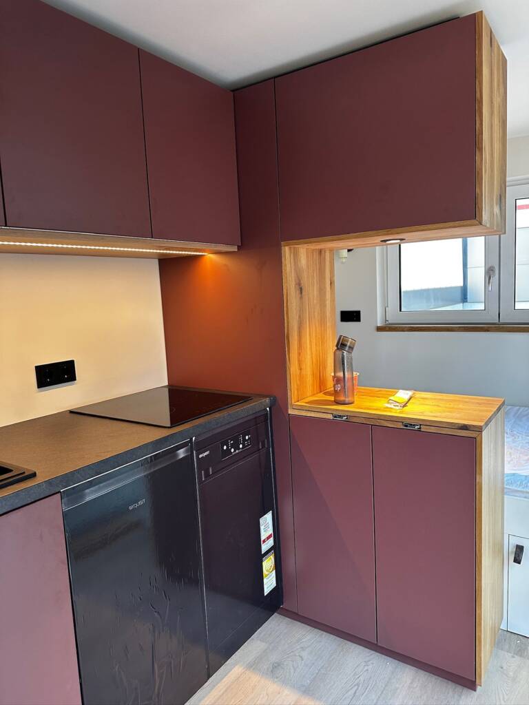 Tiny House 15 m² von Contain-us – Küchenzeile in Dunkelrot mit Kochfeld, Hängeschränken und Fenster